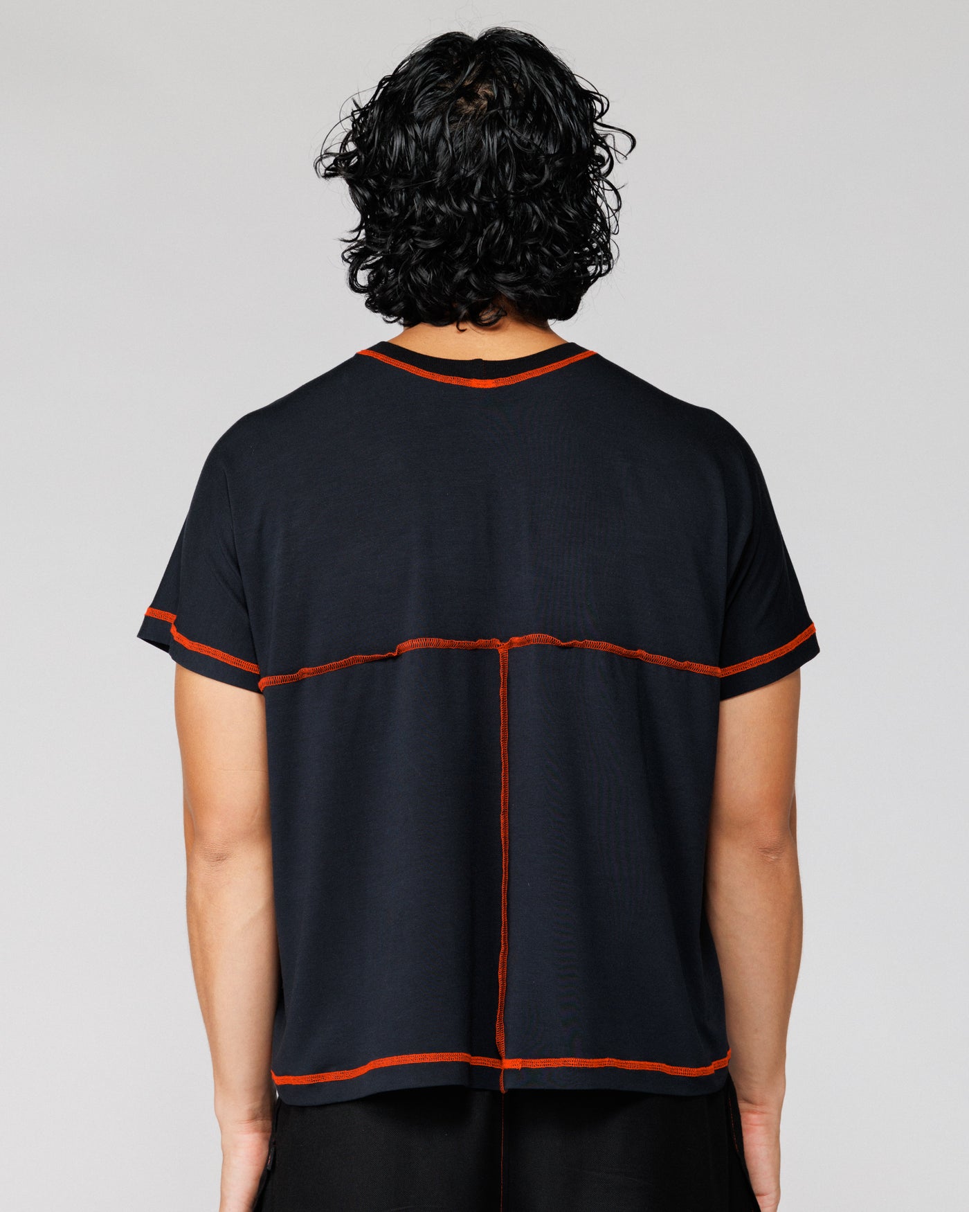 Model wearing Outnback Bog Tee in black, back view with orange cross-back seam detail