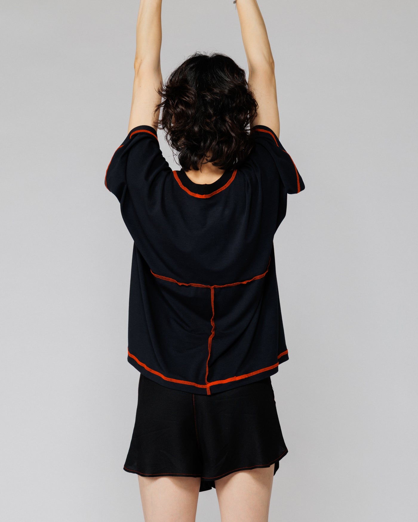 Model with arms raised in Outnback Bog Tee in black, back view showing range of movement