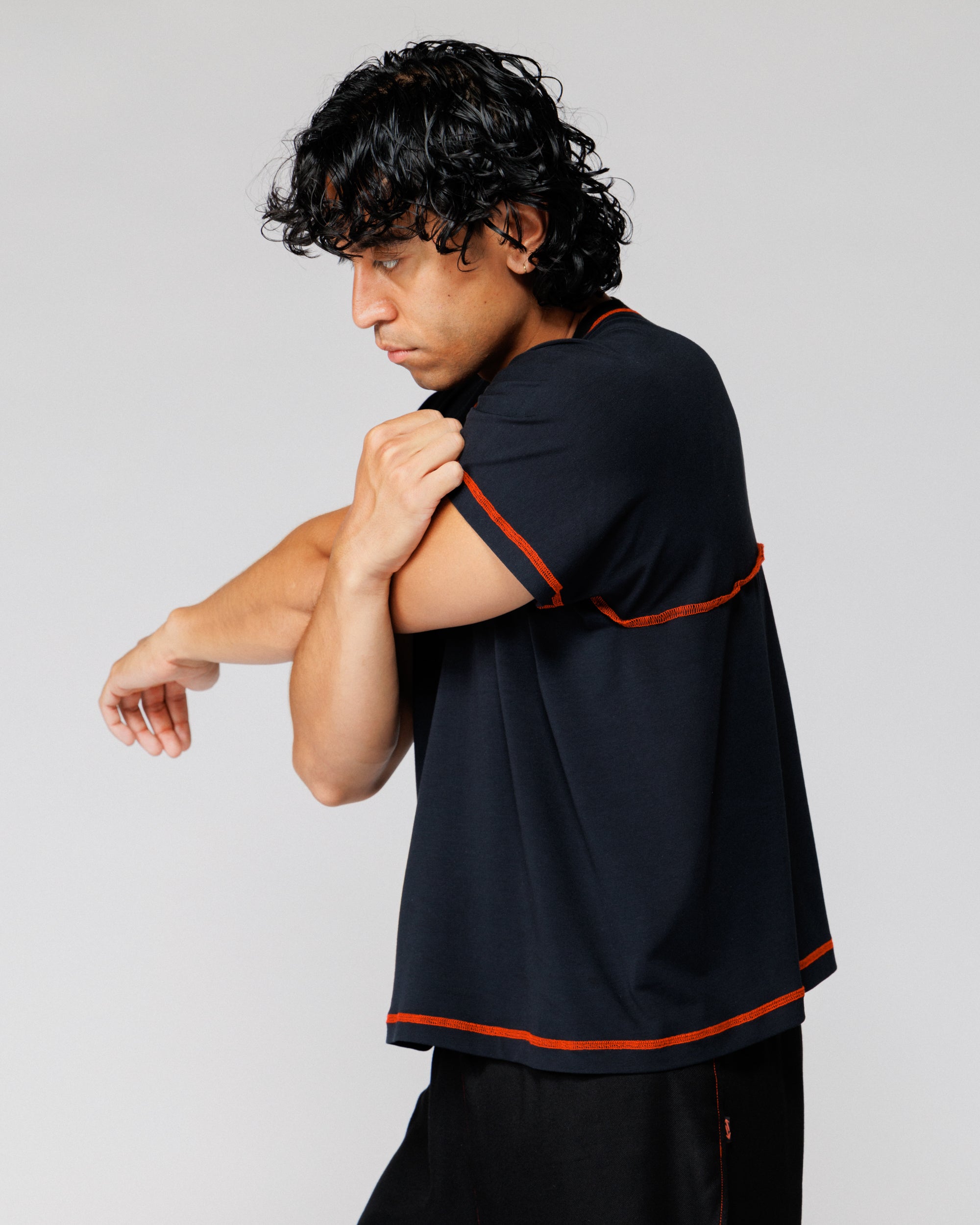Model stretching arm across chest in Outnback Bog Tee in black, rear three-quarter view