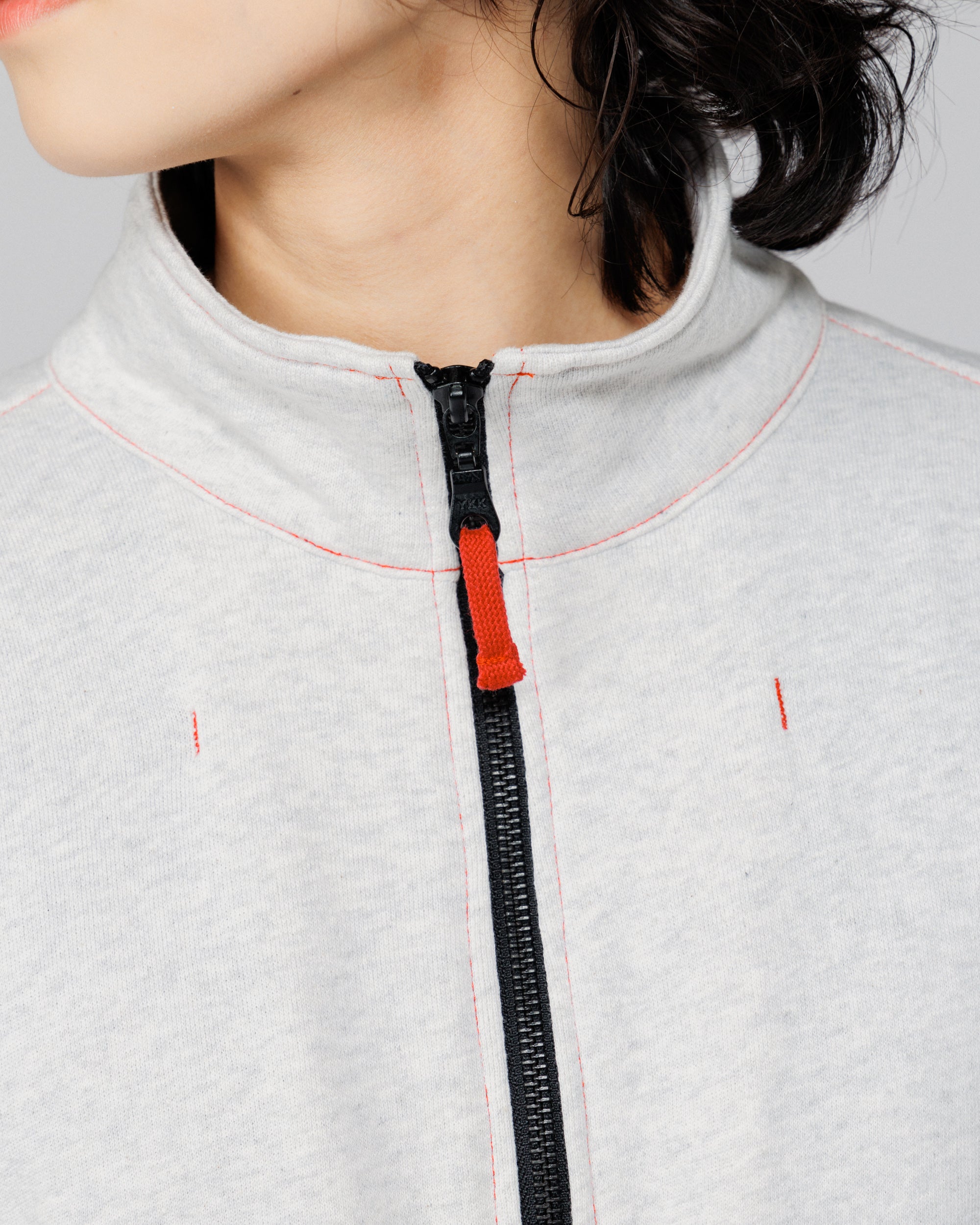 Close-up of the stand collar, front zip and red contrast topstitching on the Outnback Recovery Cape in marl grey