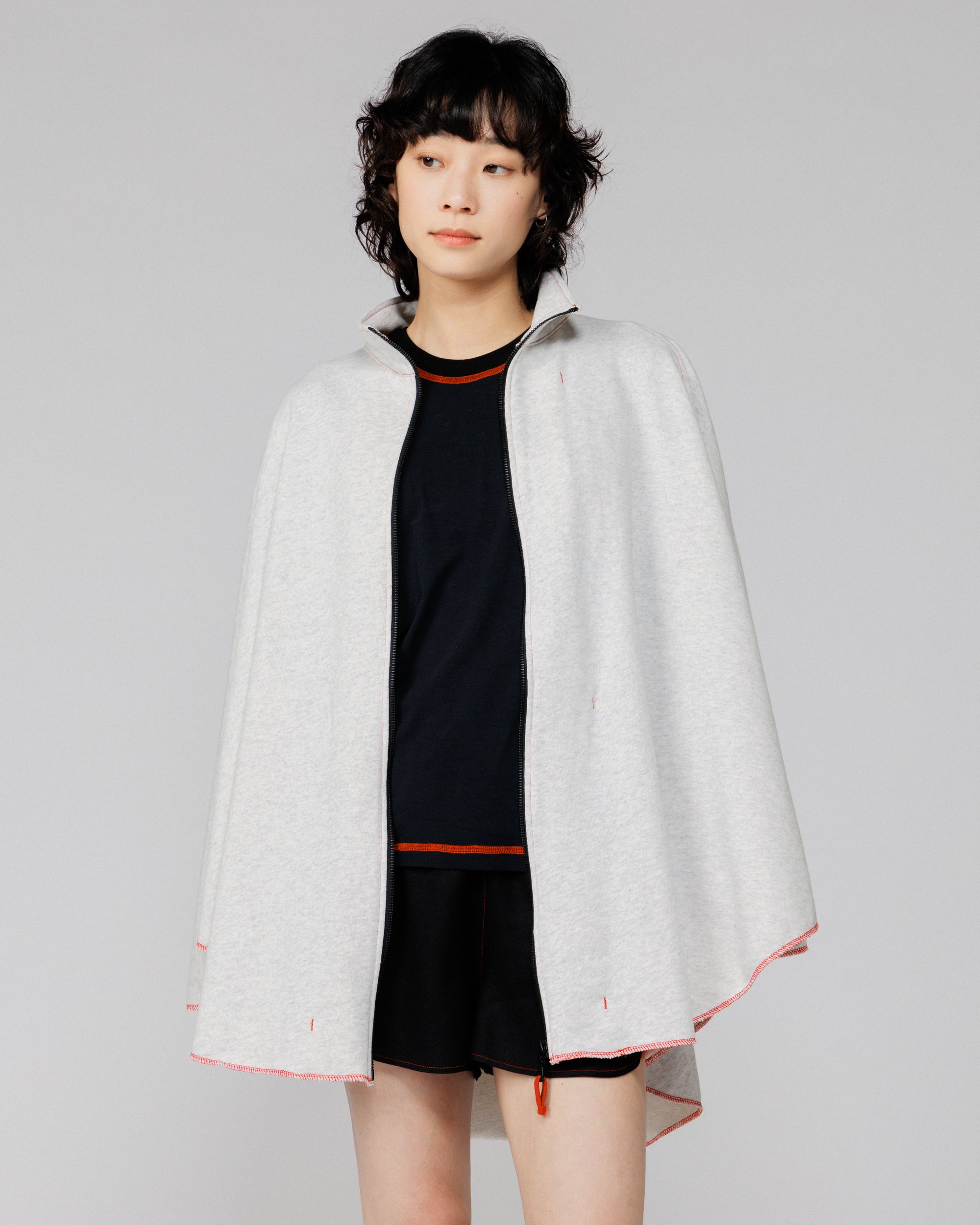Cropped view of the Outnback Recovery Cape in marl grey worn open over a black tee and shorts