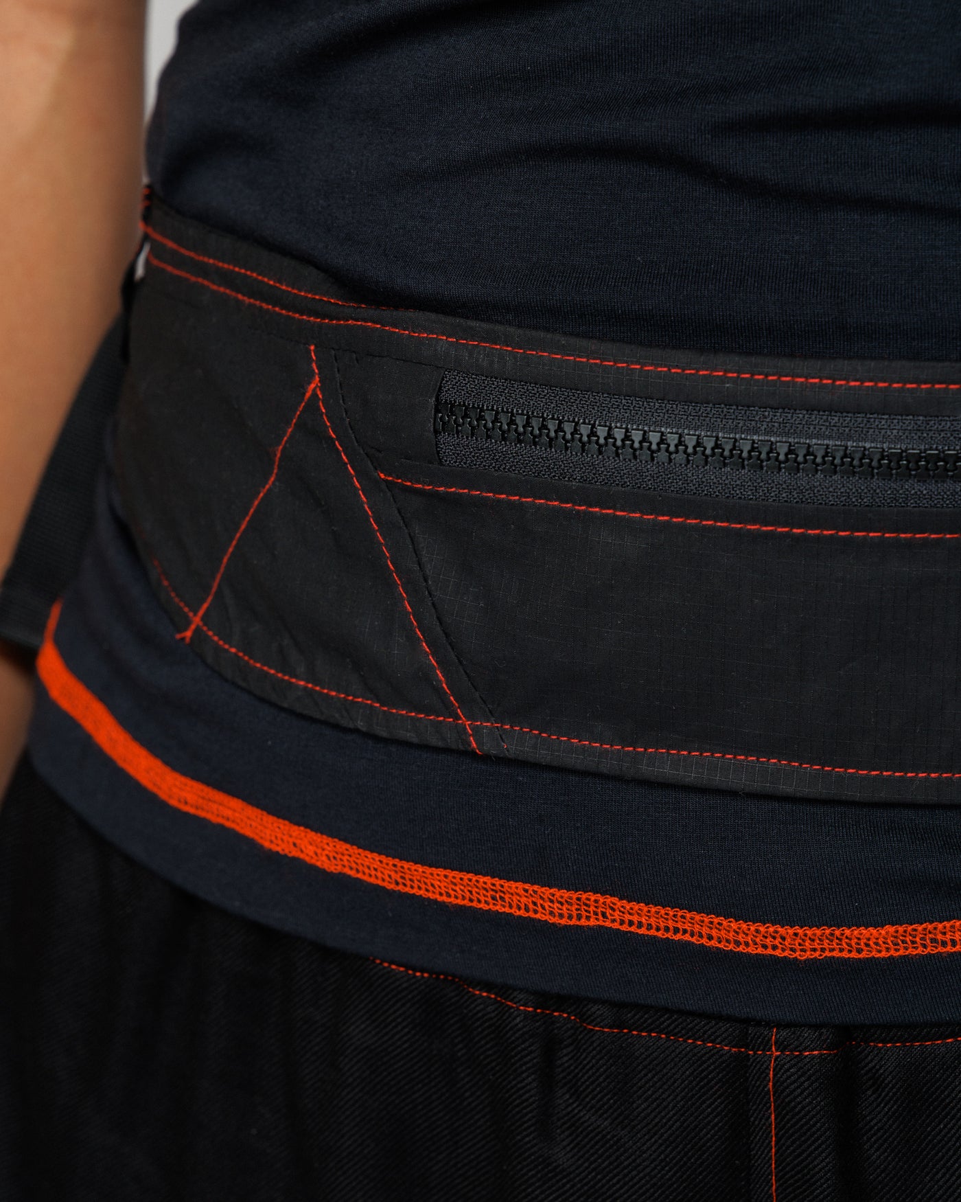 Close detail of the Outnback Running Strap in black zip pocket and red contrast stitching, worn
